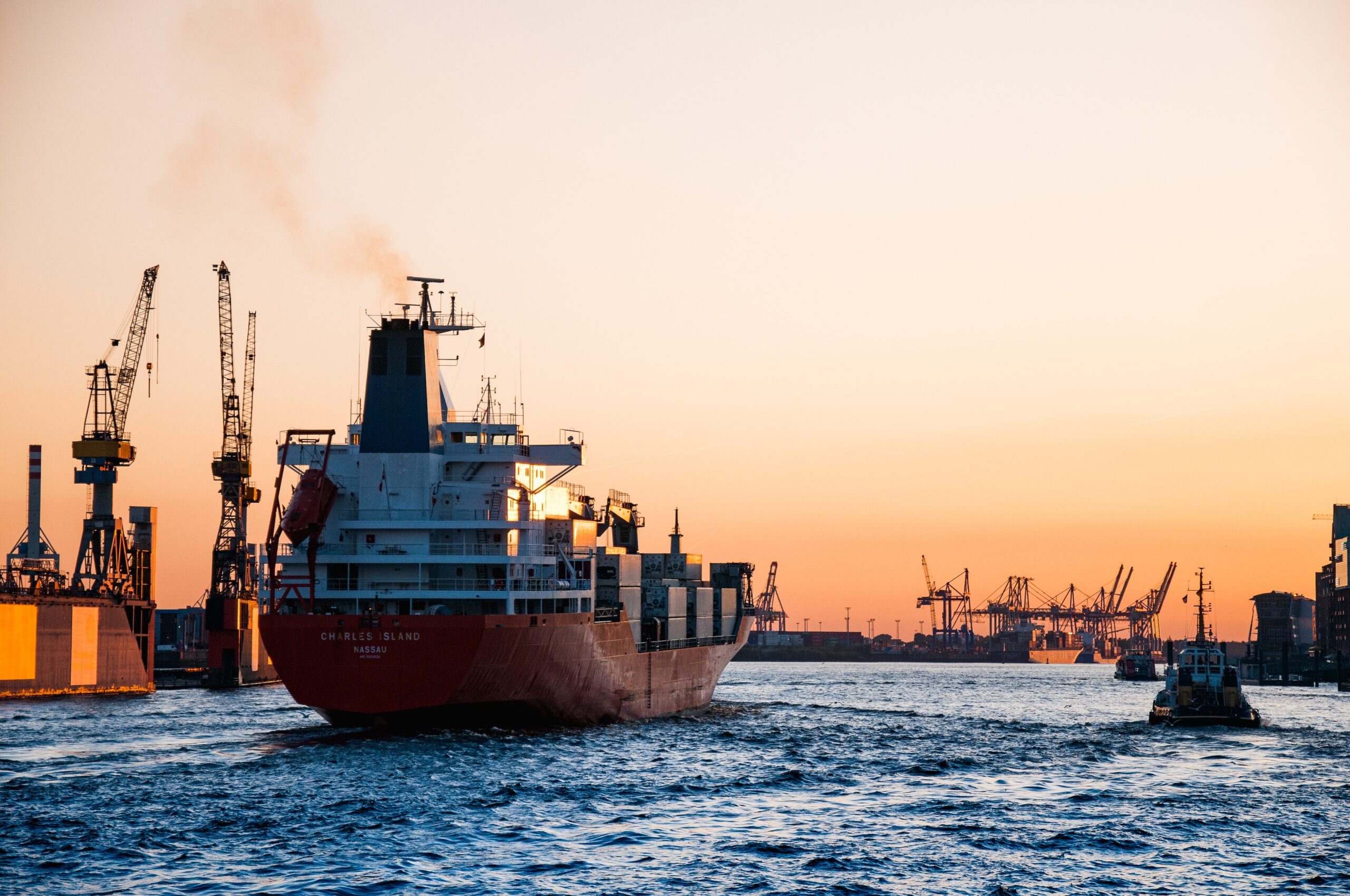 Smoky cargo ship entering container harbor.